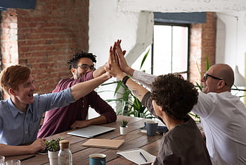 Diverse group of professionals giving a high-five in an office setting, symbolizing teamwork and success. HD wallpaper