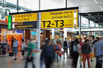 Crowded airport with motion blur and clear signage indicating baggage and arrival halls. HD wallpaper