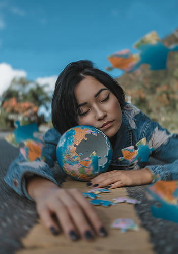A woman relaxes outdoors with a globe puzzle, capturing a moment of peaceful daydreaming. HD phone wallpaper
