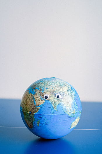 A globe with googly eyes on a blue surface symbolizes global awareness and environmental consciousness. HD phone wallpaper