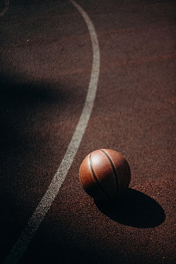 A basketball resting on an outdoor court, casting a shadow under warm daylight. HD phone wallpaper