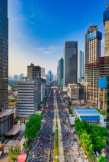 A dynamic aerial view of Jakarta showcasing modern skyscrapers and busy streets under a clear sky. HD phone wallpaper