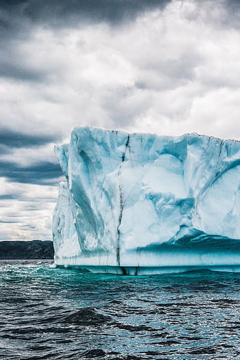 A striking graph of an iceberg in the ocean under a cloudy sky, showcasing nature's frozen beauty. HD phone wallpaper