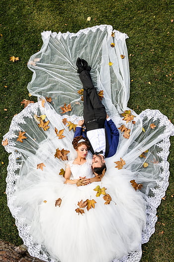 Bride and groom lying together on a lawn surrounded by autumn leaves, captured from above. HD phone wallpaper