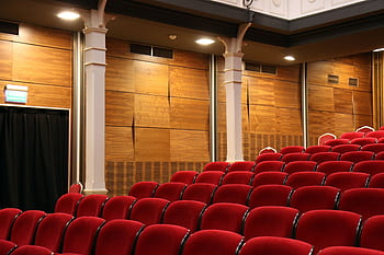 Interior of an empty auditorium with red seats and wooden panels, lit overhead. HD wallpaper