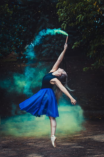 A graceful ballerina in a blue dress performs an elegant dance with colored smoke, showcasing artistic flair. HD phone wallpaper