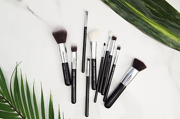 Flat lay of various makeup brushes on a marble surface with green leaves. HD wallpaper
