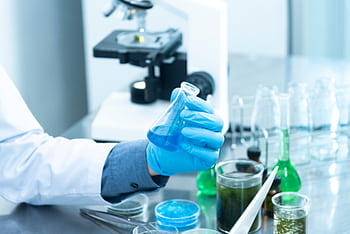 Scientist in gloves analyzing blue liquid in a laboratory setting with microscope and glassware. HD wallpaper