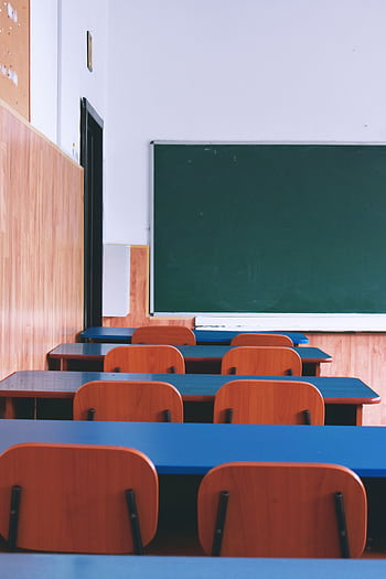 A serene view of an empty classroom with wooden desks, chairs, and a green chalkboard, capturing a quiet educational atmosphere. HD phone wallpaper