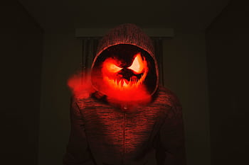 A spooky pumpkin head in a hoodie exudes a creepy Halloween vibe with red smoke. HD wallpaper