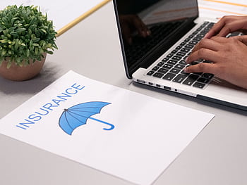 Close-up of hands typing on laptop with an insurance document visible on the desk. HD wallpaper