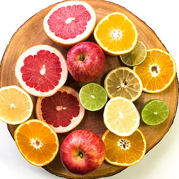 Vibrant display of sliced citrus fruits and apples on a wooden platter, emphasizing freshness and healthy eating. HD phone wallpaper