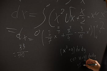 Close-up of hand writing complex math equations on a chalkboard in a classroom setting. HD wallpaper