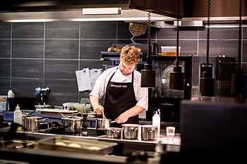 Chef preparing meal in a modern kitchen with various cookware. HD wallpaper