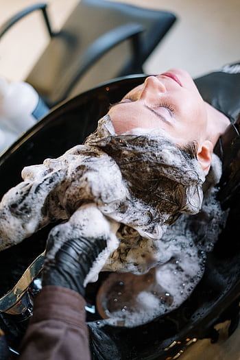 A woman getting her hair washed at a salon sink by a professional stylist wearing black gloves. HD phone wallpaper