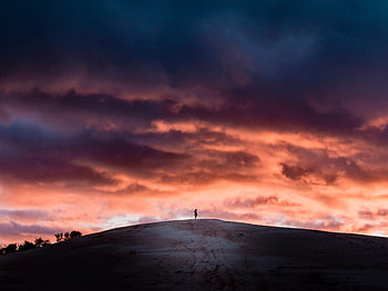 Silhouette of a person on hill under vivid sunset clouds, creating dramatic scenery. HD wallpaper