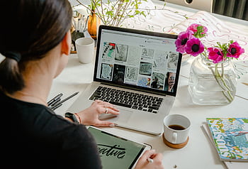 Woman in a creative workspace using a laptop and tablet for calligraphy. Artistic and tech-driven environment. HD wallpaper