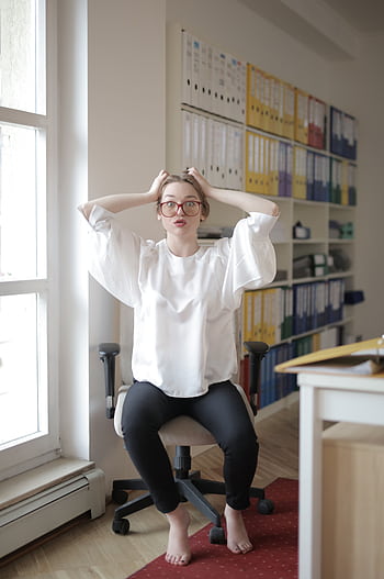 Woman in a modern office expressing frustration while seated in front of a stack of binders. HD phone wallpaper