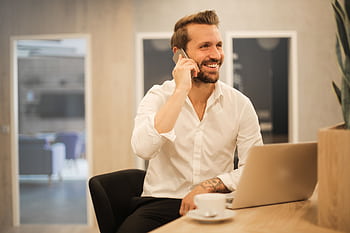 Happy businessman in white shirt on call at modern office desk with laptop. HD wallpaper