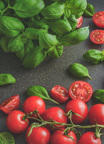 Organic basil leaves with ripe tomatoes on a rustic countertop, highlighting fresh ingredients for cooking. HD phone wallpaper