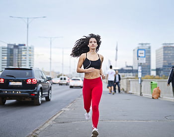 A fit woman with curly hair runs on a city street, enjoying music and staying healthy. HD wallpaper