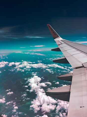 Aerial view of airplane wing over fluffy clouds with a deep turquoise sky. HD phone wallpaper