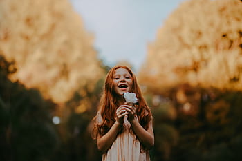 Smiling redheaded girl enjoys nature holding a flower outdoors during the day. HD wallpaper