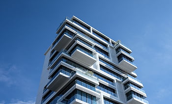 Striking low-angle shot of a modern condominium with unique balcony design and clear blue sky. HD wallpaper