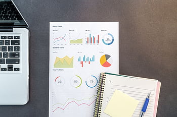 Top-down view of a desk with charts, a laptop, and notebooks, ideal for data analysis themes. HD wallpaper