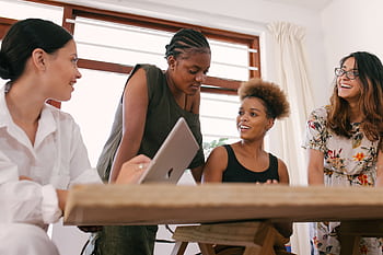 Four women in an office setting engaged in a lively creative discussion. HD wallpaper