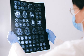 A medical professional reviewing MRI brain scans in a clinical setting, highlighting healthcare technology. HD wallpaper