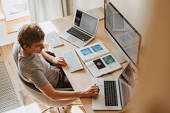 A man multitasks with laptops and a , coding in a home office setting. HD wallpaper