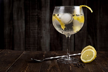 A close-up of a refreshing gin cocktail with lemon slices on a rustic wooden table, perfect for summer. HD wallpaper