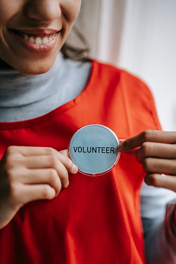 Close-up of a smiling volunteer holding a badge in a bright setting. HD phone wallpaper