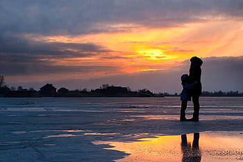 A serene sunset scene of a family silhouette on a frozen lake in Kherson, Ukraine. HD wallpaper
