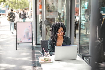 Businesswoman using a laptop at an outdoor café, enjoying a sunny day. HD wallpaper
