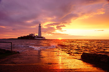 Breathtaking sunrise over a lighthouse by the sea, casting warm colors in the sky and reflecting on the water. HD wallpaper