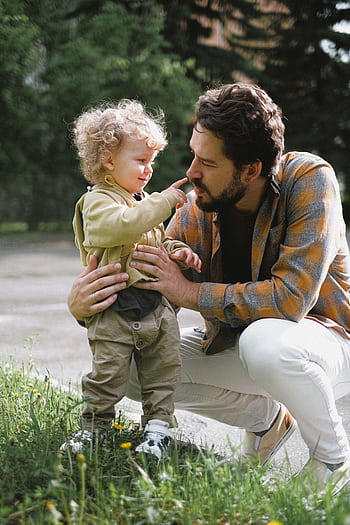 A father and his young son share a playful moment outdoors, emphasizing family and bonding. HD phone wallpaper