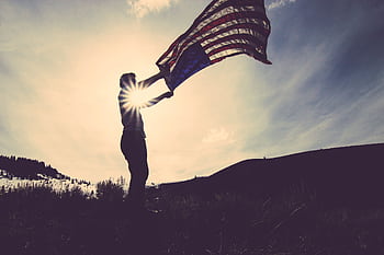 Silhouette of a person with an American flag against the bright sun in an open field. HD wallpaper
