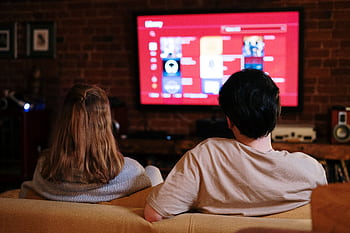 A couple enjoys streaming shows on a large TV in a cozy, brick-walled living room. HD wallpaper