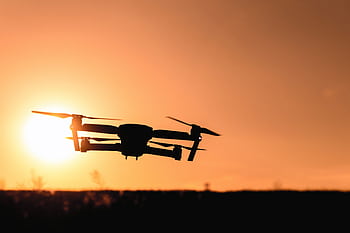 A drone in silhouette against a vibrant orange sunset sky, showcasing modern technology and aerial graphy. HD wallpaper