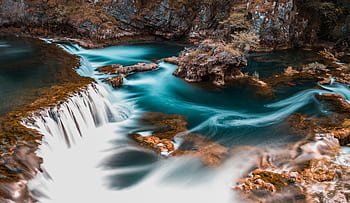 Captivating long exposure of a waterfall cascading through a tranquil rocky environment. HD wallpaper