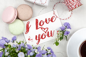 An artistic flat lay of an 'I Love You' card surrounded by macarons, flowers, and coffee, perfect for Valentine's Day. HD wallpaper