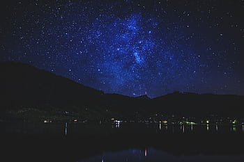 A breathtaking view of a starry night sky with mountain silhouettes reflected in a calm lake. HD wallpaper