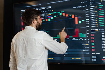A man analyzes cryptocurrency graphs on a touchscreen monitor in a modern office setting. HD wallpaper