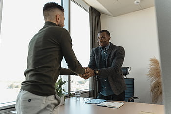 Two businessmen exchanging a handshake during a professional meeting in a modern office setting. HD wallpaper