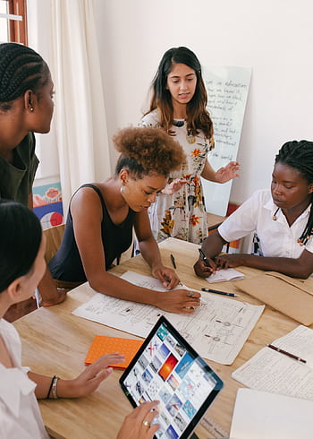 Group of women collaborating on a creative project in a modern office environment. HD phone wallpaper