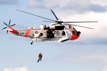 A rescue helicopter from the Royal Norwegian Air Force performs a hoist operation mid-air on a clear day. HD wallpaper