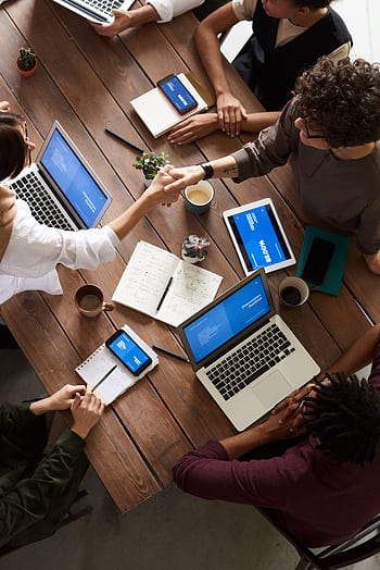A diverse group of professionals brainstorming in a modern workspace with laptops and notebooks. HD phone wallpaper