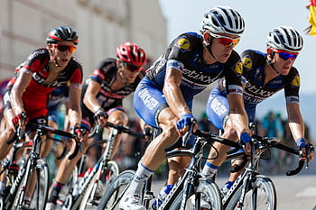 Competitive cyclists in a high-speed race, showcasing athleticism and teamwork. HD wallpaper